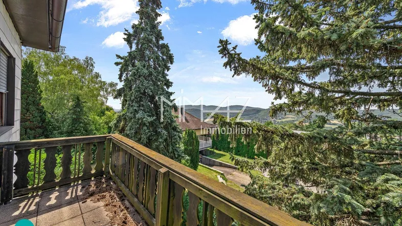 Alter Balkon mit Holzbalkongeländer und weitem Blick über die grüne Landschaft.