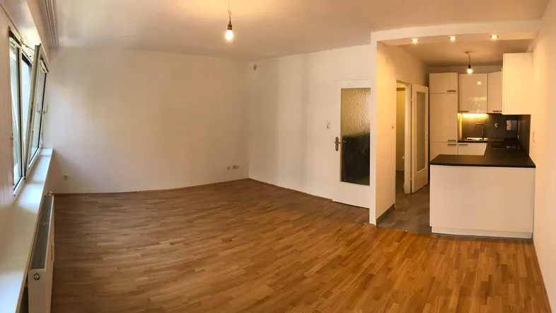 Geräumiger Wohnbereich mit hellem Parkettboden und offener Verbindung zur modernen Küche.