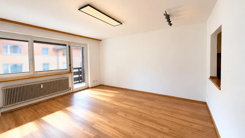 Helles Wohnzimmer mit Laminatboden, großem Fenster und Zugang zum Balkon.
