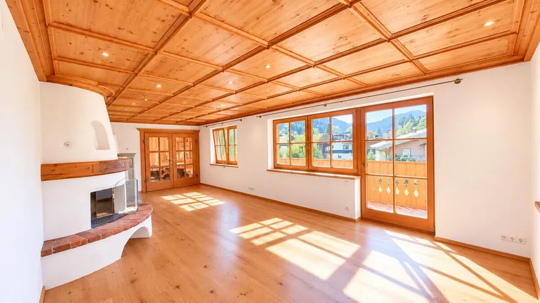 Helles Wohnzimmer mit Holzbalkendecke, Kamin und Zugang zum Balkon, bietet viel natürliches Licht.