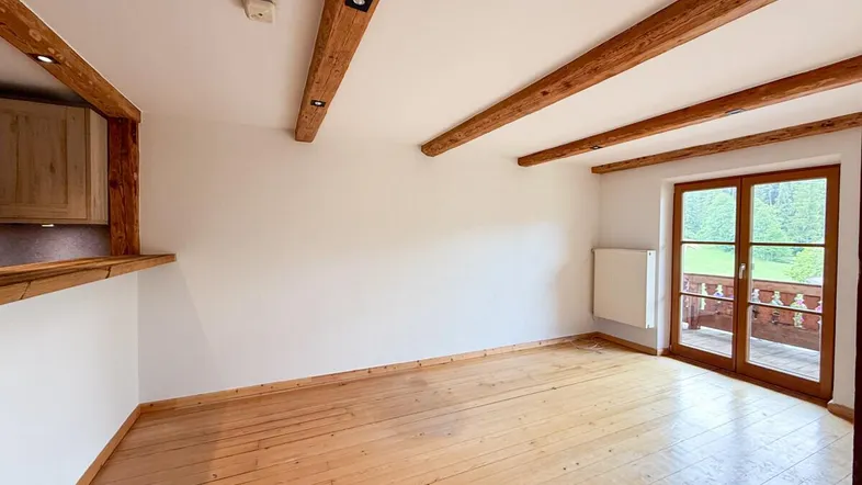Helles Zimmer mit Holzbalken, Holzboden und Zugang zu einem Balkon mit Bergblick.