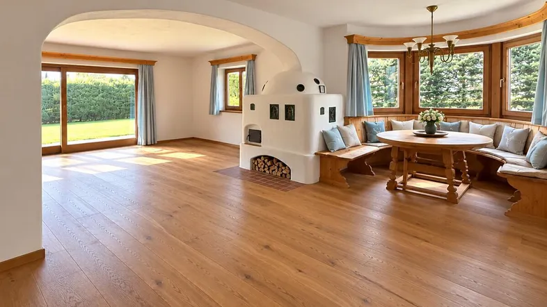 Helles Wohn- und Esszimmer mit traditionellem Kachelofen, Holzboden und Zugang zum Garten.