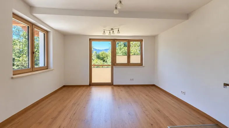 Helles Wohnzimmer mit Holzboden und Zugang zu einem französischen Balkon mit Bergblick.