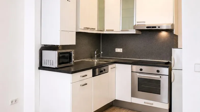 Moderne Einbauküche mit weißen Schränken, dunkler Arbeitsplatte und integrierten Geräten.