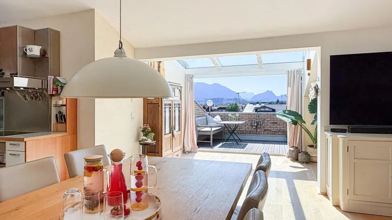 Heller Essbereich mit Holztisch, Blick auf die Terrasse und die umliegende Berglandschaft.