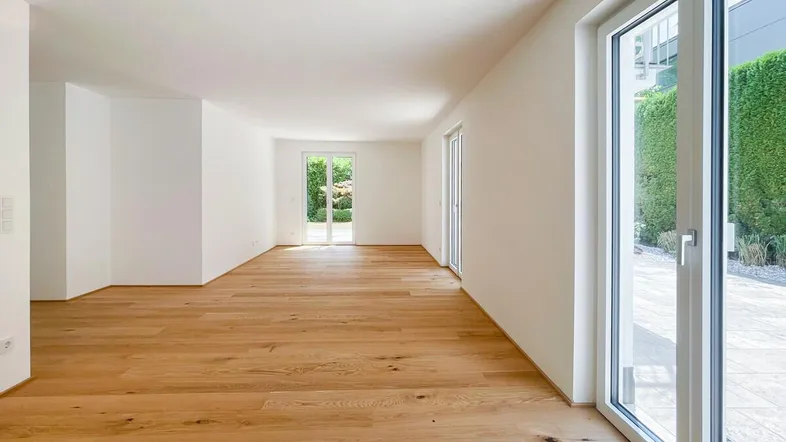 Helles, leeres Zimmer mit Holzboden und Zugang zu einer Terrasse oder Gartenbereich.
