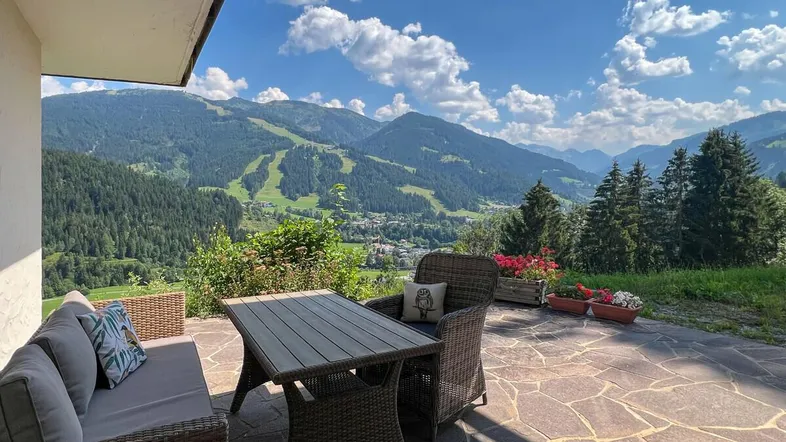 Geräumige Terrasse mit bequemen Gartenmöbeln und atemberaubendem Bergblick unter blauem Himmel.