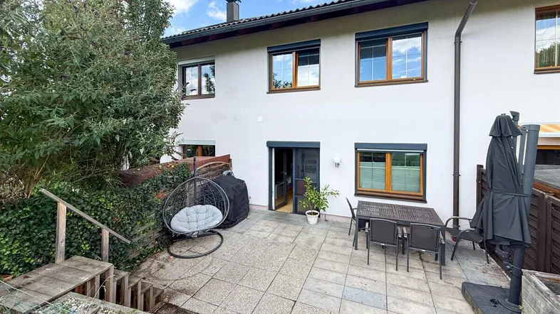 Gepflasterte Terrasse mit Gartenmöbeln und Zugang zum Haus, umgeben von Grün.