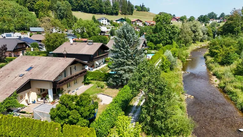 Luftaufnahme eines Wohngebiets mit Häusern, viel Grün und einem Flusslauf.