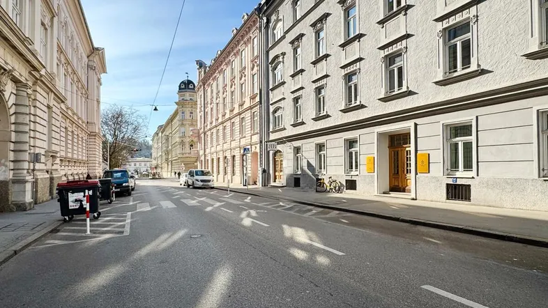 Blick auf eine belebte Straße mit historischen Gebäuden und geparkten Autos unter blauem Himmel.