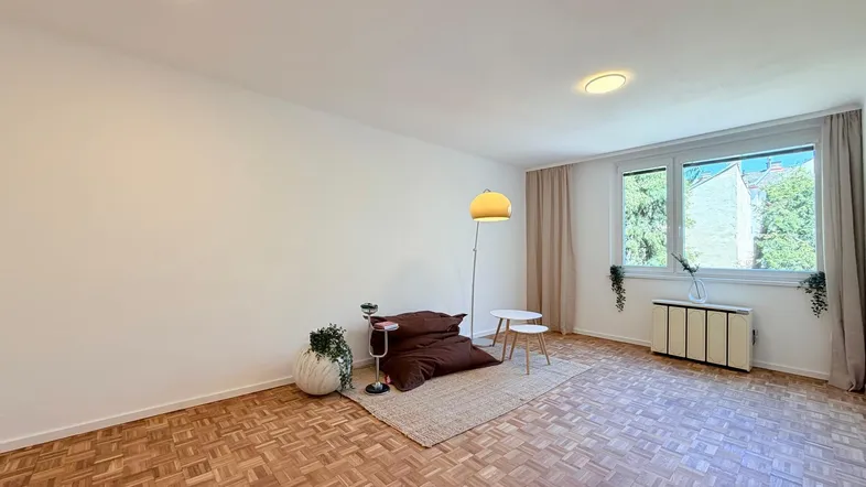 Helles Zimmer mit Parkettboden, großen Fenstern und minimalistischer Einrichtung, ideal als Wohnbereich.