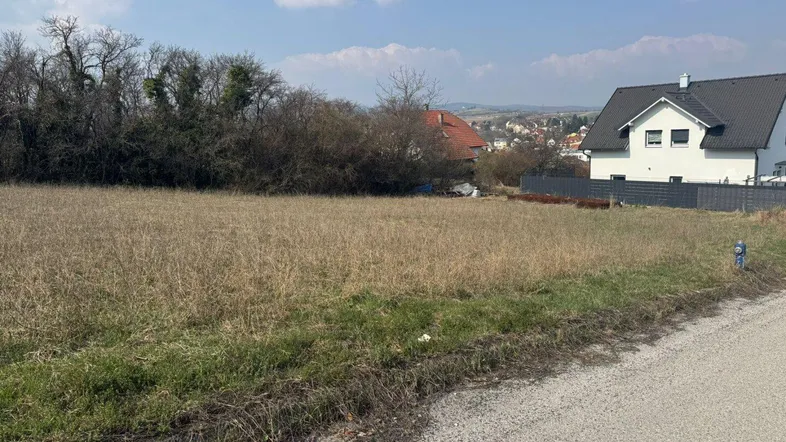 Unbebautes Grundstück mit Blick auf die umliegende Wohnsiedlung und Landschaft unter blauem Himmel.
