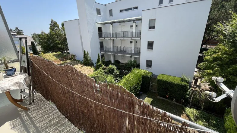 Blick von einer Loggia mit Bambuszaun auf ein modernes Apartmentgebäude und den grünen Innenhof.