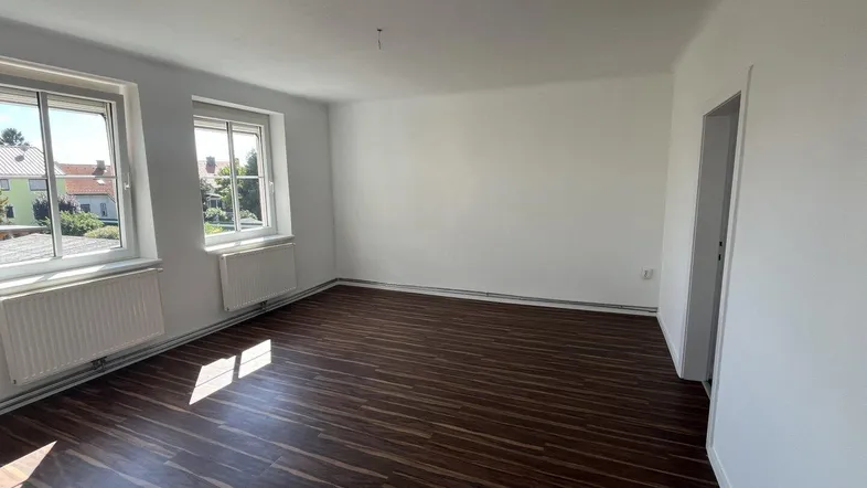 Helles Zimmer mit dunklem Laminatboden, weißen Wänden und einem angenehmen Blick ins Grüne.