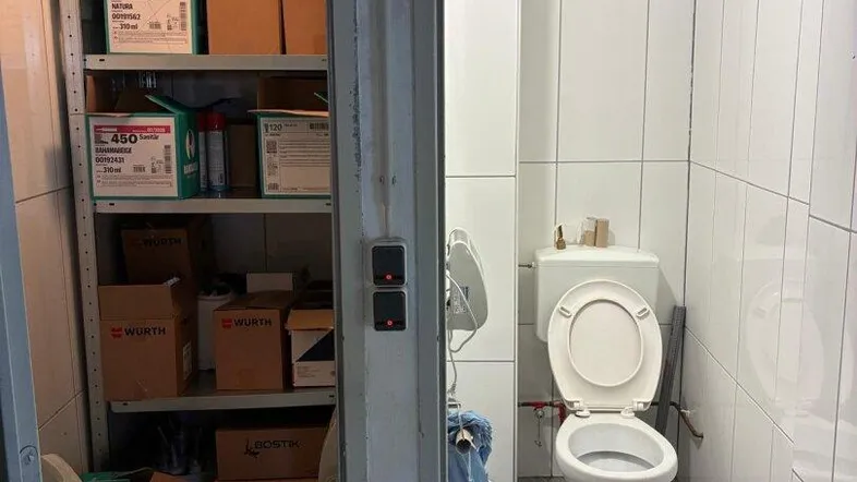 Blick durch zwei offene Türen in einen Lagerraum mit Regalen und eine kleine Toilette mit Fliesen.
