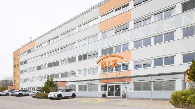 Großes Bürogebäude mit moderner Fassade, vielen Fenstern und Parkplätzen vor dem Eingangsbereich.