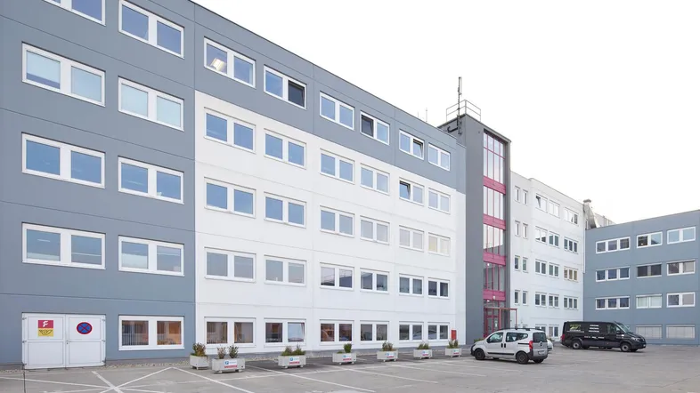 Modernes Geschäftsgebäude mit blaugrauer und weißer Fassade sowie Parkplätzen davor und einem Eingangsbereich.