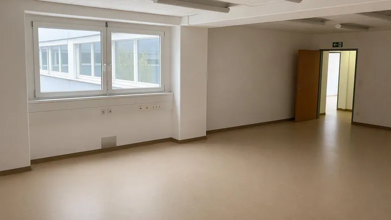Geräumiger, leerer Büroraum mit großen Fenstern, hellem Vinylboden und weißen Wänden.