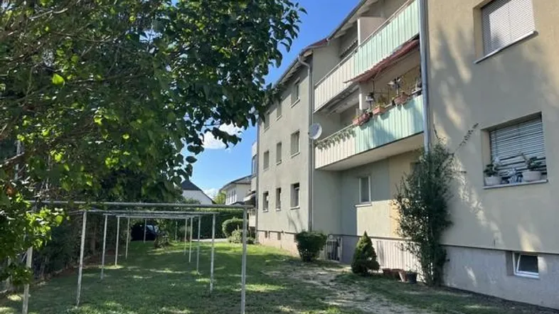 Mehrfamilienhaus mit Balkonen und einem grünen Gartenbereich unter blauem Himmel.