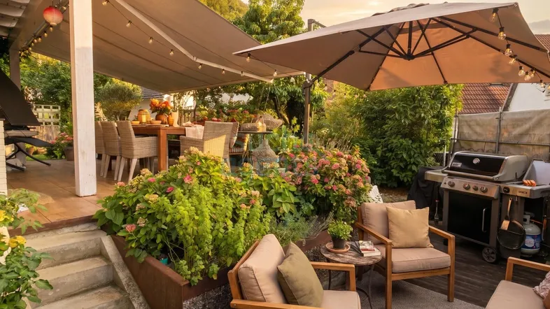Großzügige Terrasse mit Essbereich unter Markise, Lounge-Möbeln, Grill und üppiger Bepflanzung für entspannte Stunden im Freien.
