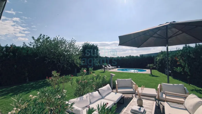 Großer Garten mit Rasenfläche, Pool und gemütlicher Lounge-Sitzgruppe im Freien unter Sonnenschirm.