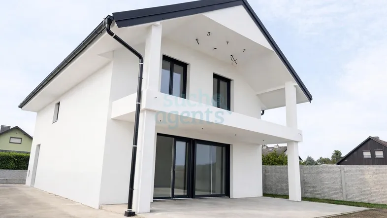 Modernes weißes Einfamilienhaus mit schwarzem Dach, Balkon und großer Terrasse im Bauzustand.