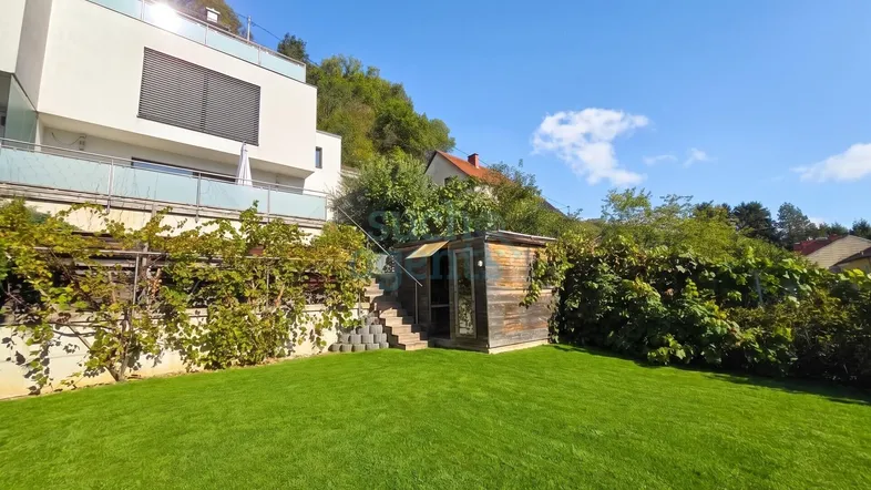 Grüner Gartenbereich mit Rasenfläche, kleinem Holzschuppen und Blick auf die umliegende Natur.