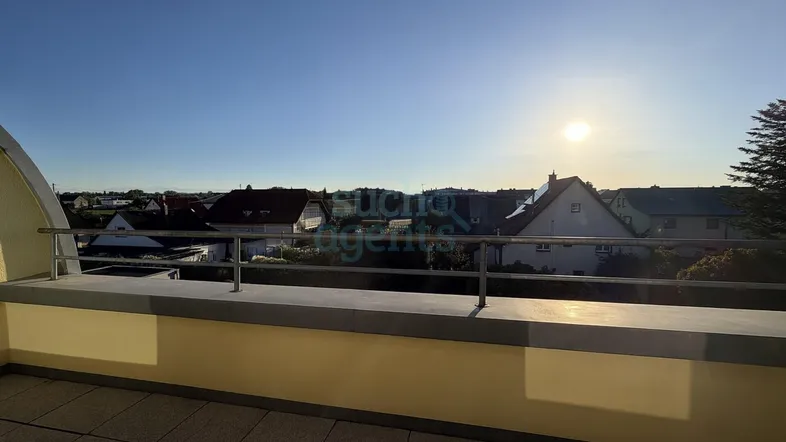 Geräumiger Balkon mit Fliesenboden und weitem Blick über die Dächer bei Sonnenuntergang.