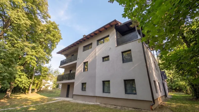 Modernes Mehrfamilienhaus mit Balkonen, umgeben von viel Grün und Bäumen.