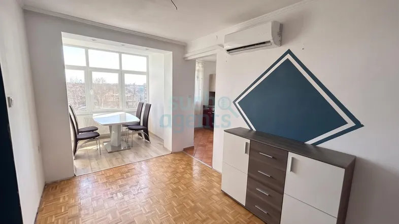 Heller Wohnbereich mit Parkettboden, modernem Sideboard und offenem Zugang zum Essbereich mit großem Fenster.