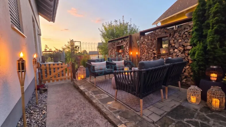Abendliche Terrasse mit gemütlichen Sitzmöbeln, Holzstapel und stimmungsvoller Beleuchtung.
