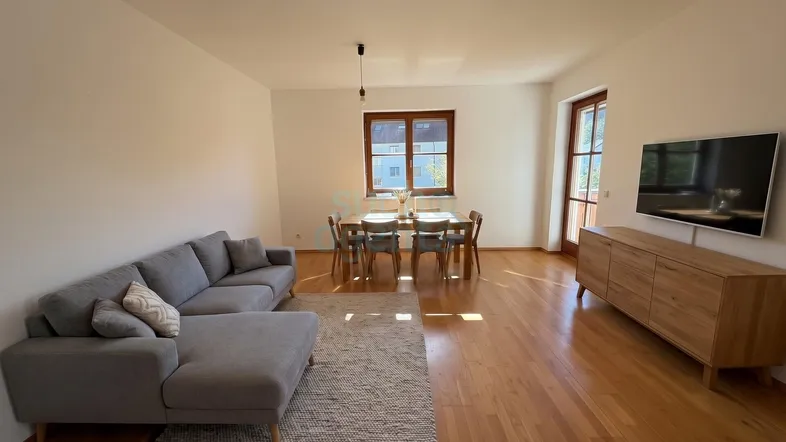 Heller offener Wohn- und Essbereich mit Holzfußboden, moderner Einrichtung und Zugang zum Balkon.