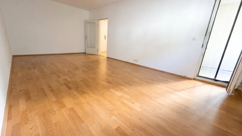 Helles, leeres Wohnzimmer mit Parkettboden und Zugang zu einem Balkon, bereit zur individuellen Gestaltung.