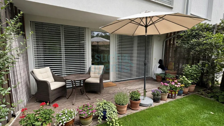 Gemütliche Terrasse mit Holzboden, Gartenmöbeln und vielen Pflanzen, ideal zum Entspannen im Freien.