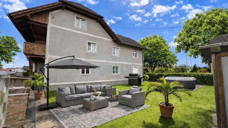 Sonniger Gartenbereich mit gemütlicher Lounge-Ecke, Grill und Whirlpool vor dem traditionellen Haus.