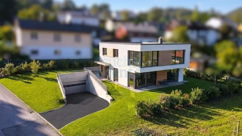 Modernes Einfamilienhaus mit großen Fenstern, umgeben von einer gepflegten Grünfläche und integrierter Tiefgarage.