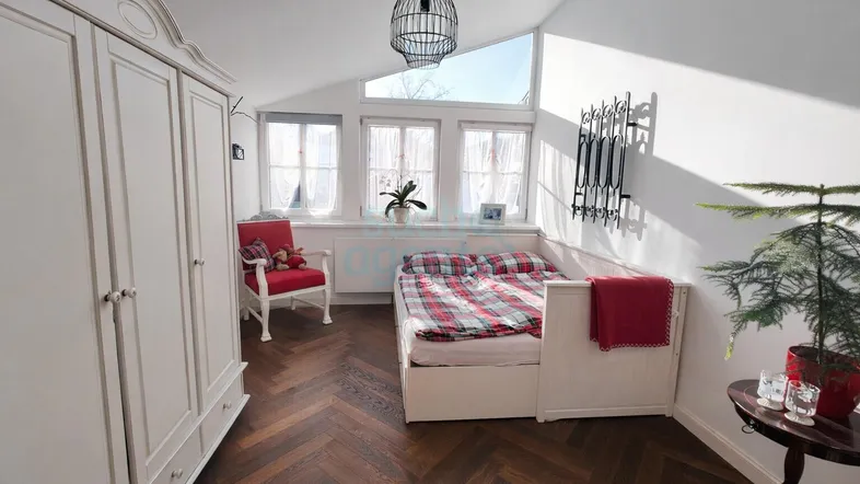 Ein helles Schlafzimmer mit schrägem Dach, Holzboden und einem gemütlichen Bett mit karierter Bettwäsche.