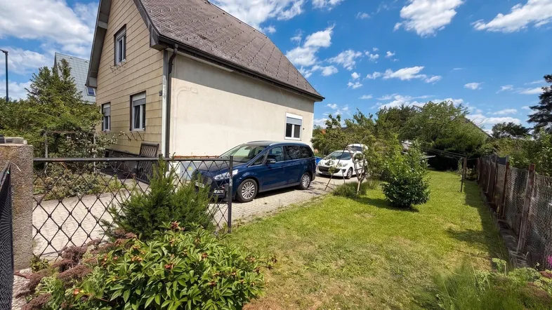 Einfamilienhaus mit Satteldach, Vorgarten und Stellplätzen im Freien unter blauem Himmel.