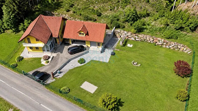 Luftaufnahme eines gepflegten Hauses mit großem Garten, Auffahrt und angrenzendem Waldgebiet.