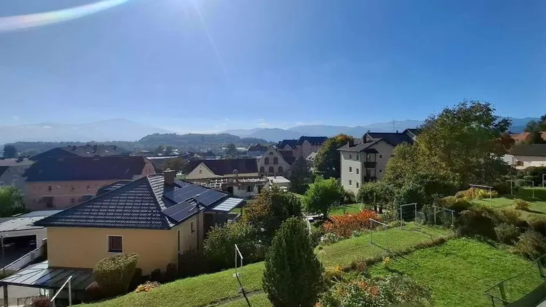 Sonnige Aussicht auf eine ländliche Umgebung mit Häusern und Bergen im Hintergrund.