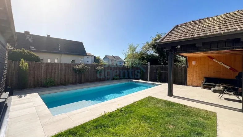 Sonniger Gartenbereich mit modernem Pool und angrenzendem Lounge-Bereich unter einem Holzpavillon.