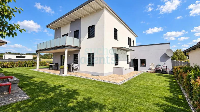 Modernes Einfamilienhaus mit gepflegtem Garten, Balkon und Terrasse unter blauem Himmel.