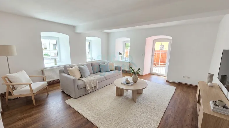 Helles Wohnzimmer mit Holzboden, bequemer Couch und Zugang zu einem kleinen Balkon.