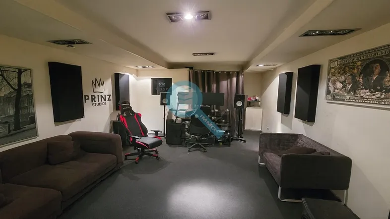 Geräumiger Raum, eingerichtet als Musik- oder Gaming-Studio, mit bequemen Sofas, Gaming-Stuhl und Akustikpaneelen.