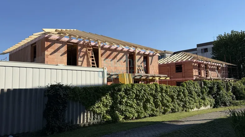Zwei im Bau befindliche Wohnhäuser mit sichtbaren Ziegelwänden und Holz-Dachkonstruktionen unter blauem Himmel.