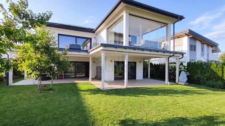 Modernes Einfamilienhaus mit großer Rasenfläche und verglastem Obergeschossbereich.