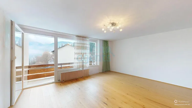Heller, leerer Raum mit Holzboden, Zugang zum Balkon und malerischem Bergblick.