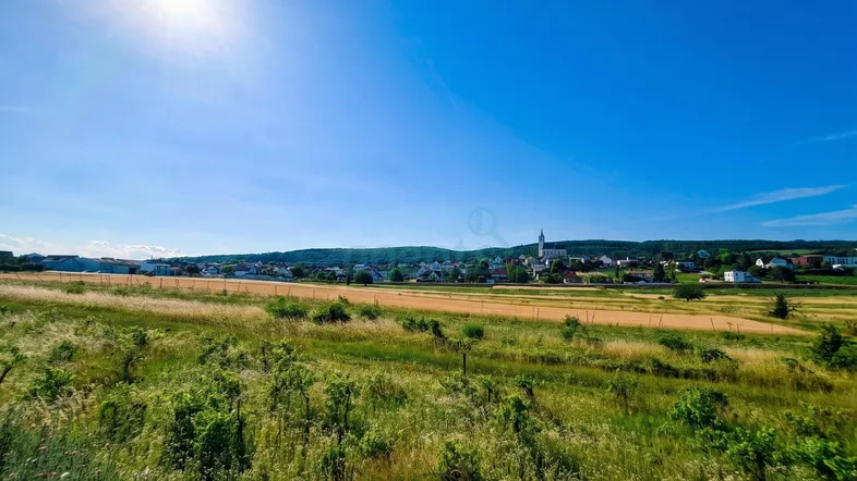 Sonniger Blick über weite Felder und Weinberge auf ein charmantes Dorf in der Ferne.