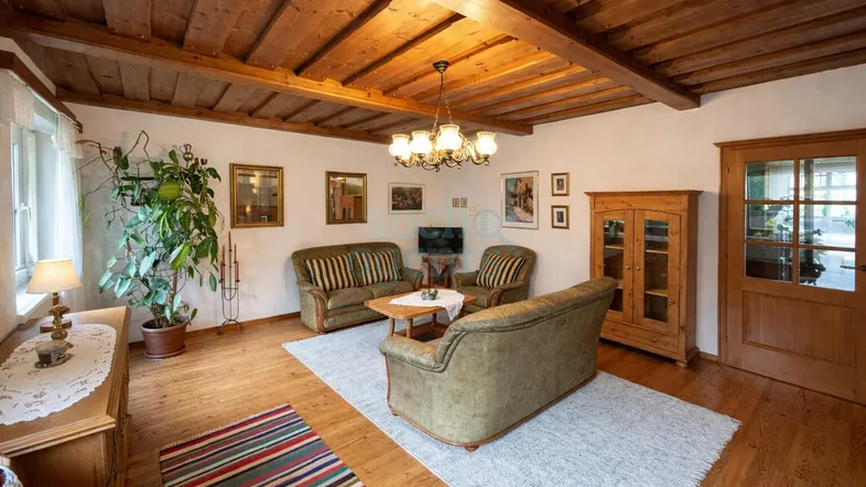 Gemütliches Wohnzimmer mit sichtbaren Holzbalken an der Decke, Dielenboden und traditionellen Möbeln.