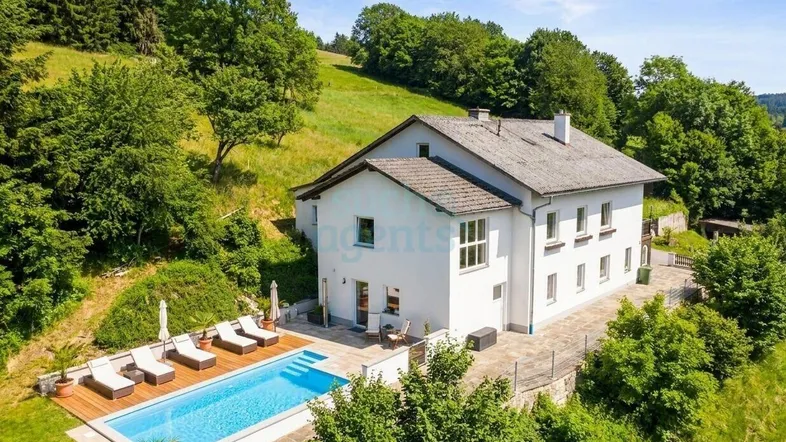Idyllisches Anwesen mit weißem Haus, großem Pool und Sonnenterrasse inmitten grüner Hügellandschaft.
